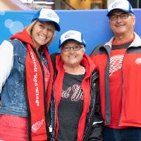 Three alumni pose together, wearing their Red Wings GVSU hats at the Detroit Red Wings GVSU Night